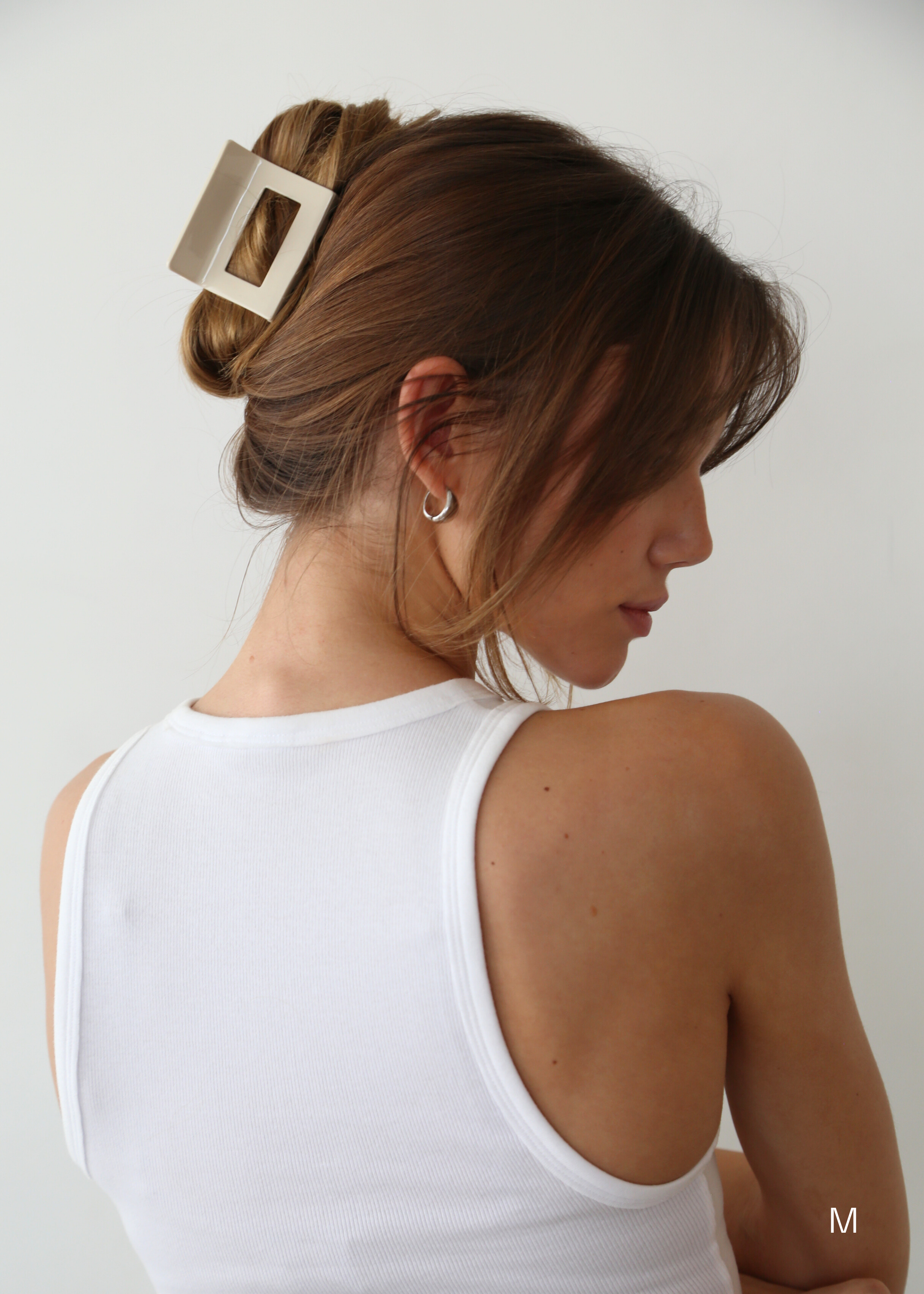 Side view of woman with chestnut coloured hair in an up do secured with a medium sized beige coloured hair claw clip wearing a white tank top