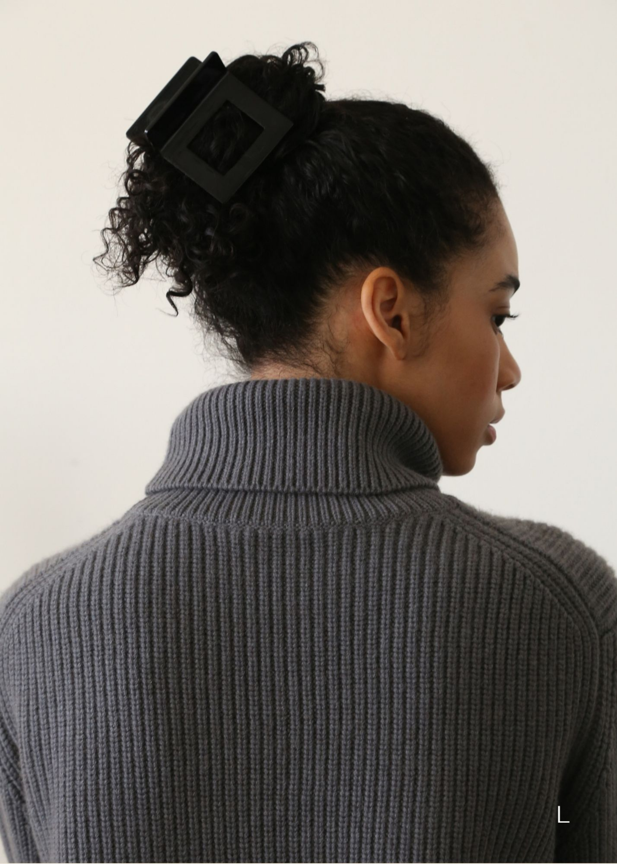 Woman wearing a grey night turtle neck sweater with black curly hair styled in an updo secured with a large black, square shaped hair claw clip