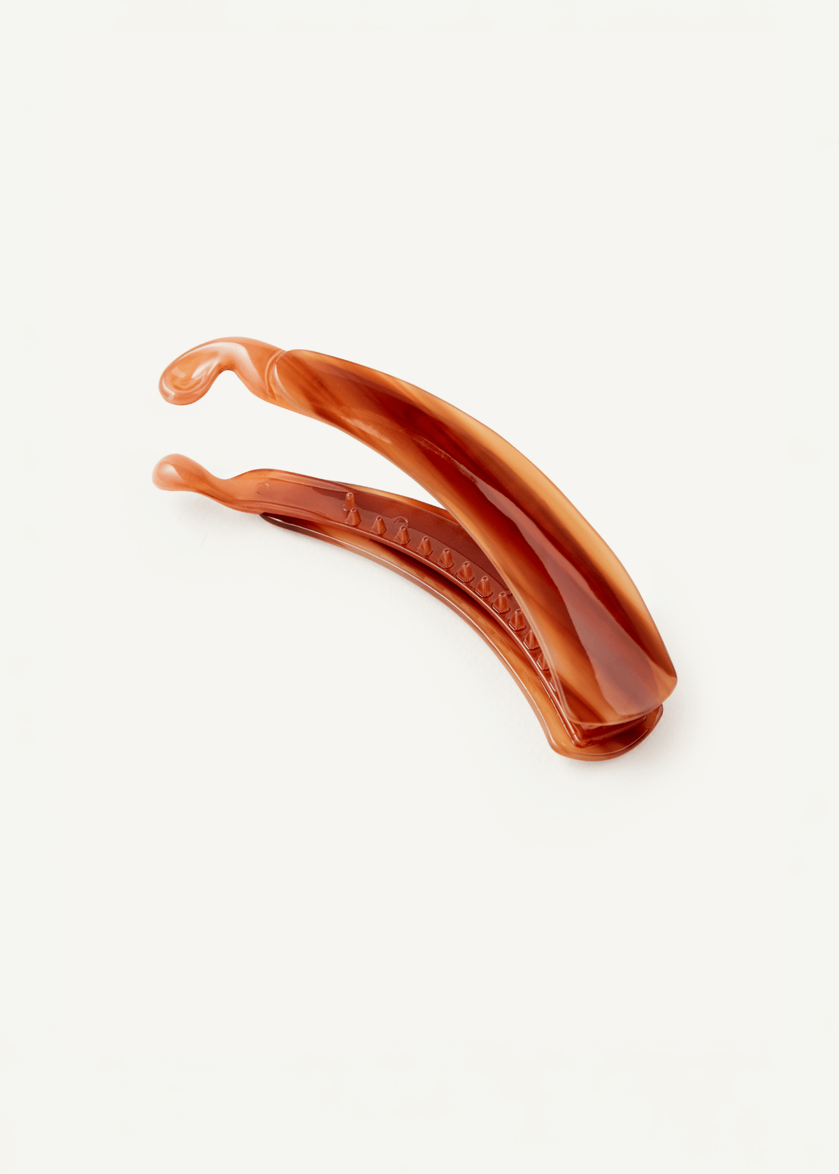A claw clip in a warm amber-brown colour, photographed on a clean white background, showing the internal teeth of the clip.