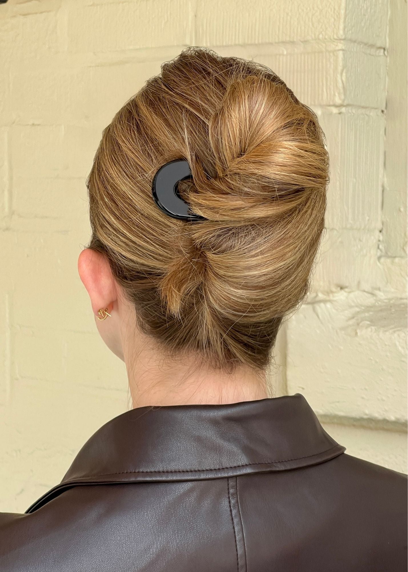 Woman with blonde hair styled in a french twist secured by a french pin against a neutral background