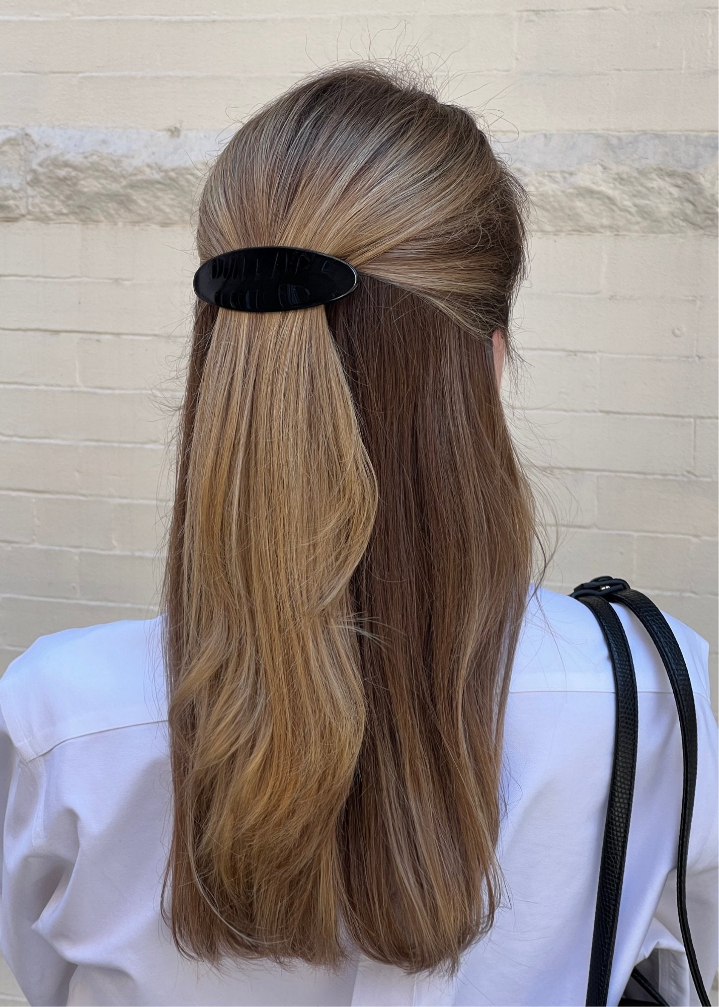 Woman with long, blonde hair using a black barrette against a light background