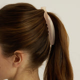 Person with a ponytail held by a pink banana hair clip against a plain background