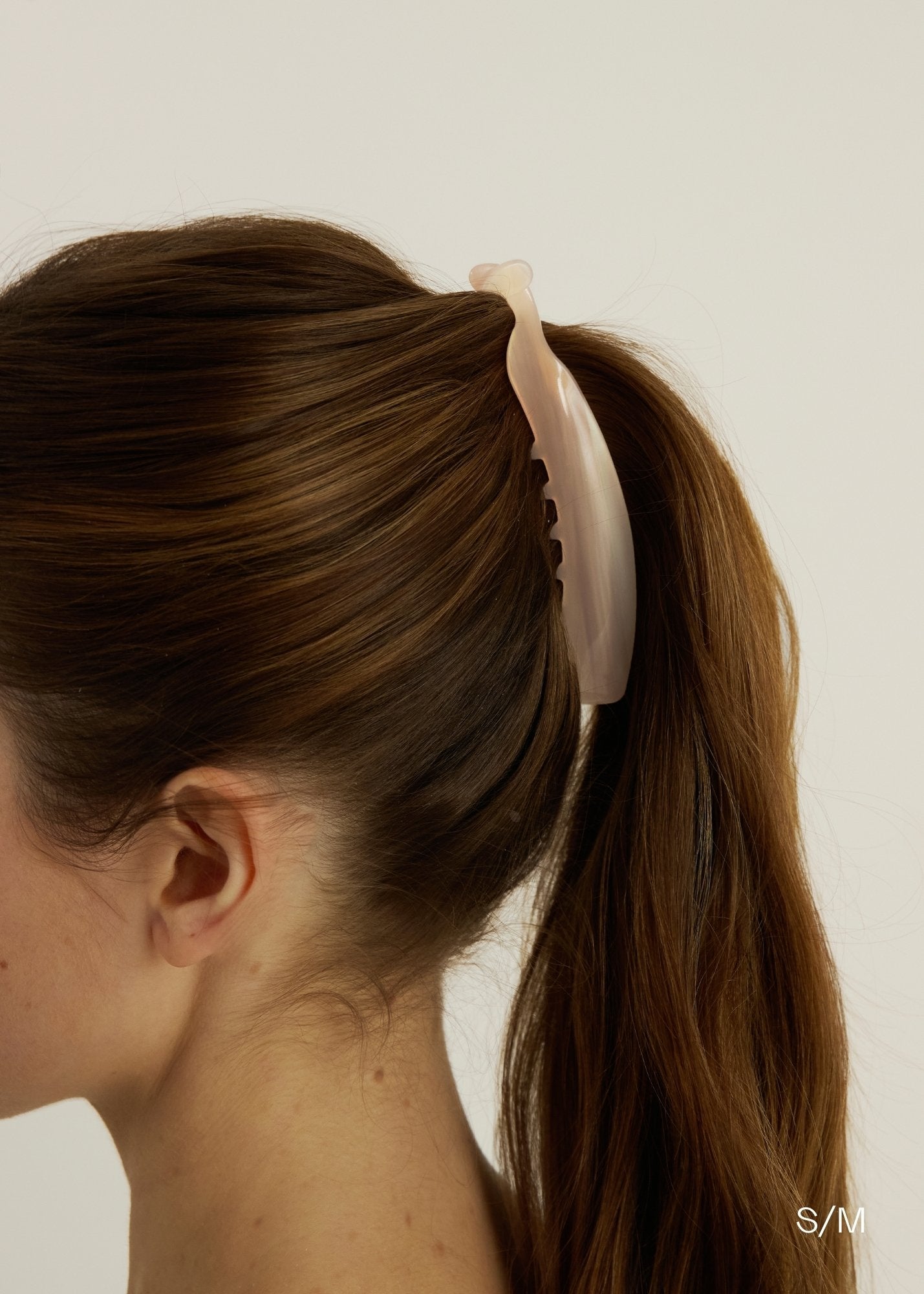 Person with a ponytail held by a pink banana hair clip against a plain background