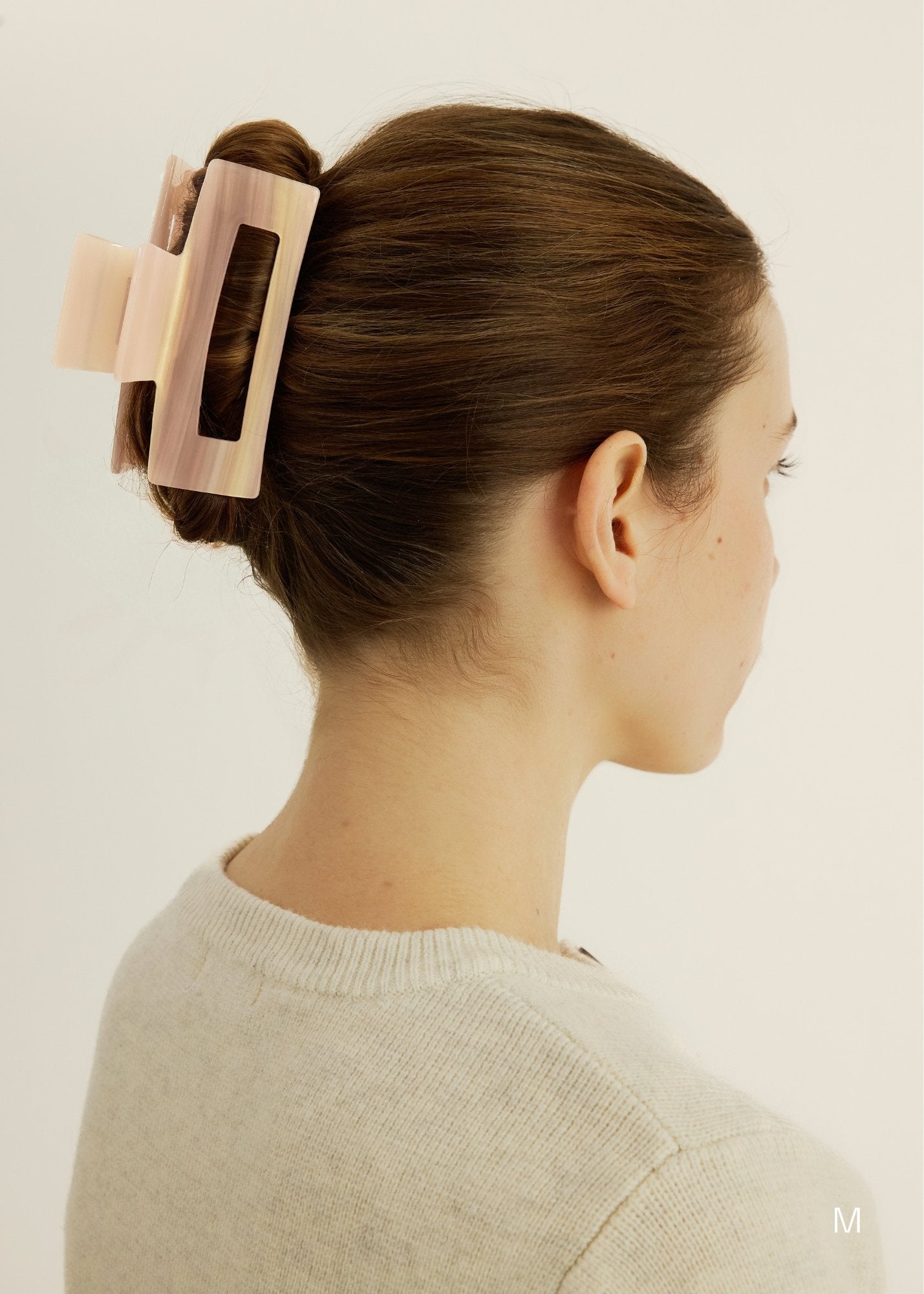 Woman with a pink hair clip in her brown hair against a plain background