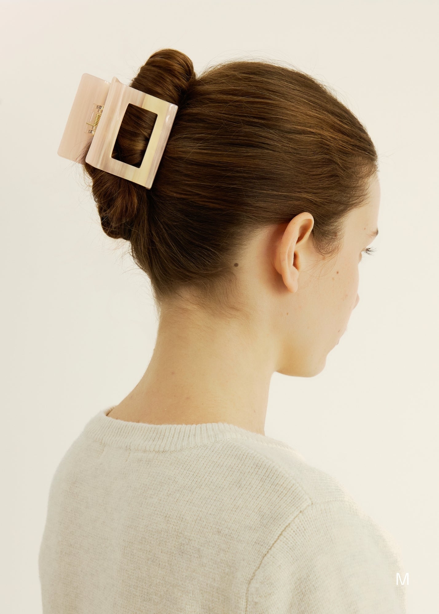 Woman with an up-do hairstyle held by a pink hair clip against a plain background