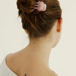 A woman with brown hair styled in a bun secured with a pink hair clip on a plain background