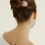 A woman with brown hair styled in a bun secured with a pink hair clip on a plain background