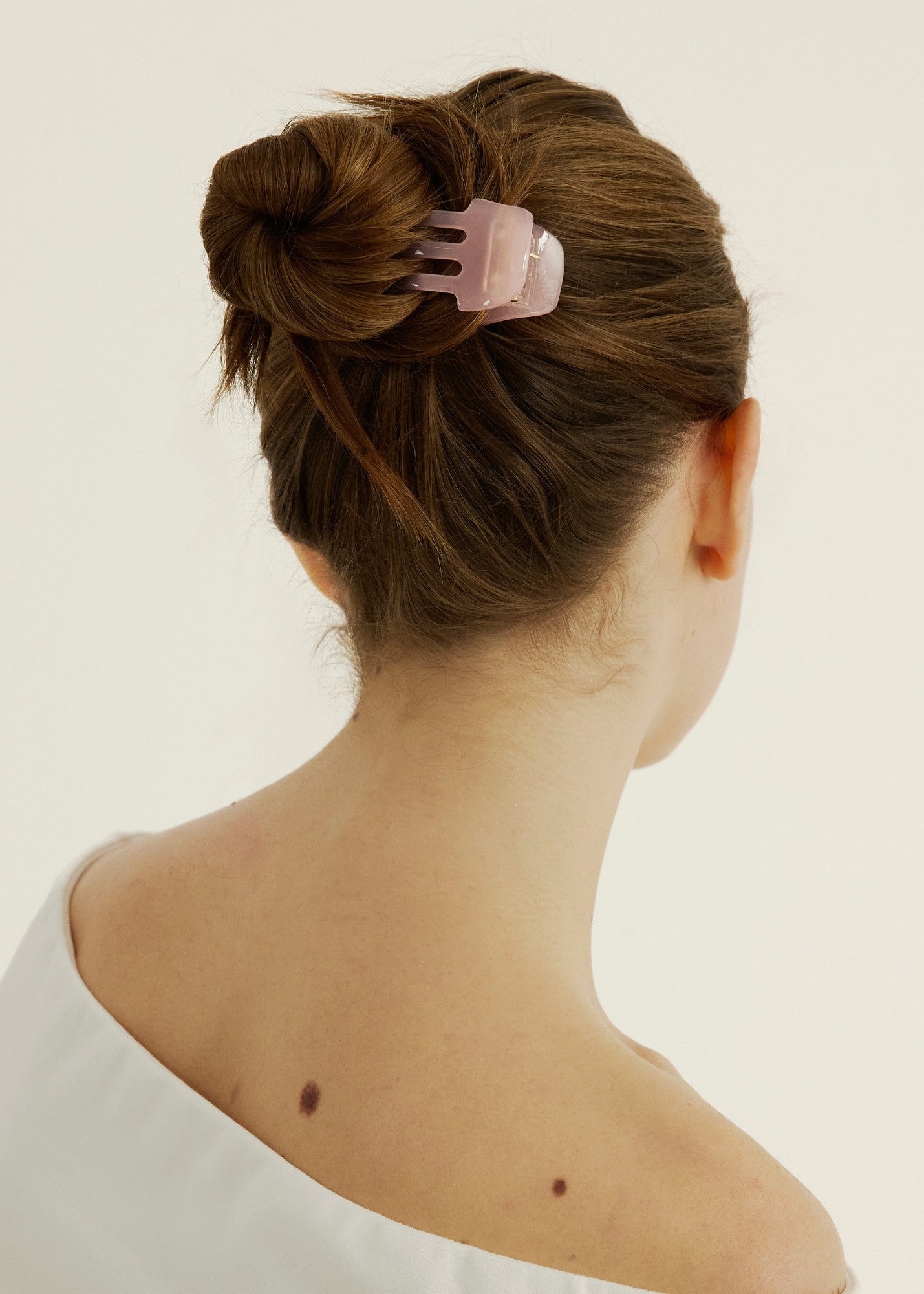 A woman with brown hair styled in a bun secured with a pink hair clip on a plain background
