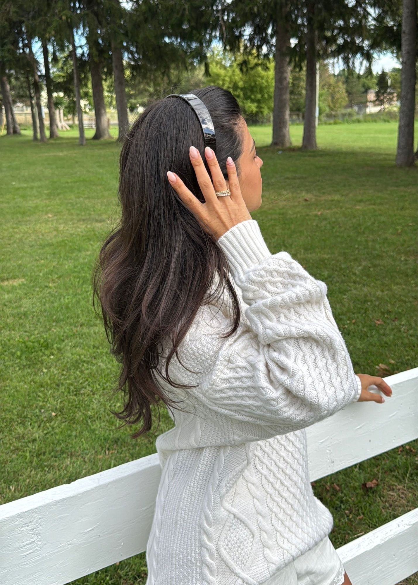 Woman in a white cable knit sweater standing in a park wearing the Easy Headband in Cider