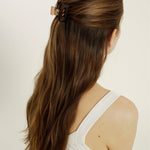 Woman with long brown hair styled half-up, half-down secured with a transparent, brown mini hair clip against a plain background