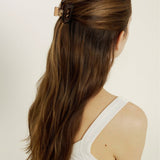 Woman with long brown hair styled half-up, half-down secured with a transparent, brown mini hair clip against a plain background