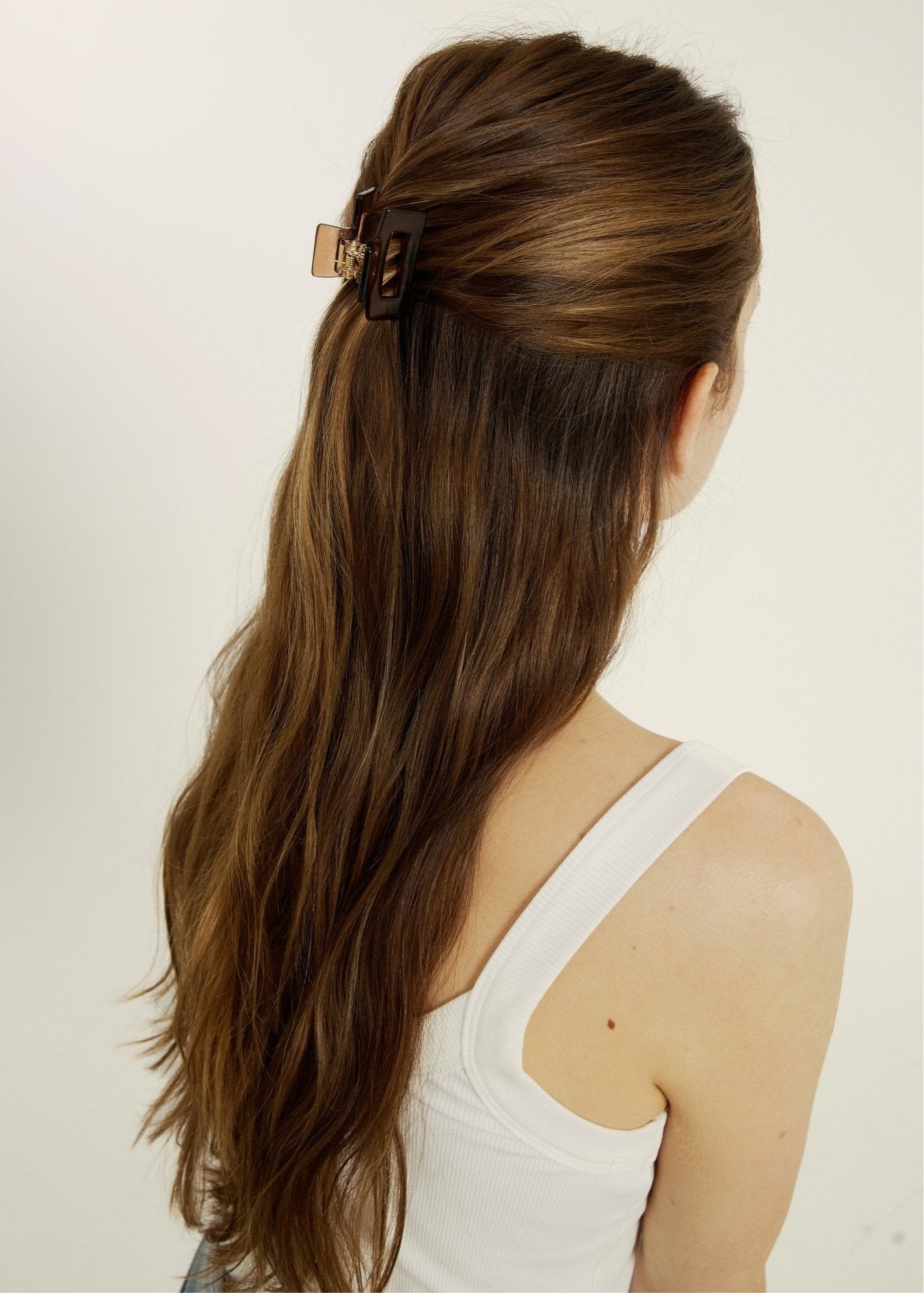 Woman with long brown hair styled half-up, half-down secured with a transparent, brown mini hair clip against a plain background