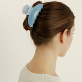 Woman with an up-do hairstyle secured with a medium-sized light blue claw clip against a plain background