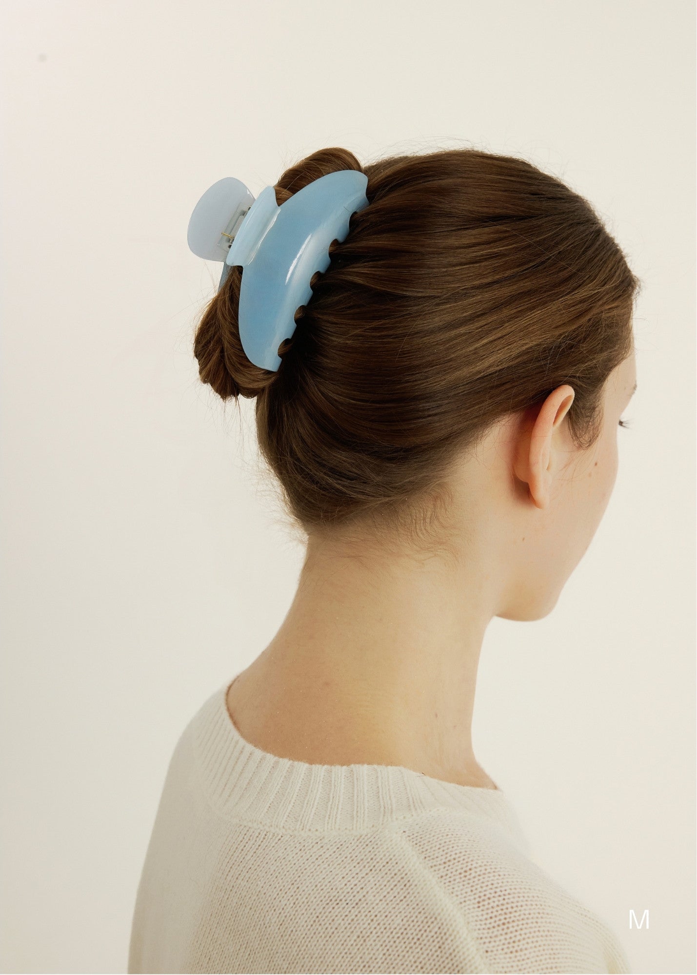 Woman with an up-do hairstyle secured with a medium-sized light blue claw clip against a plain background