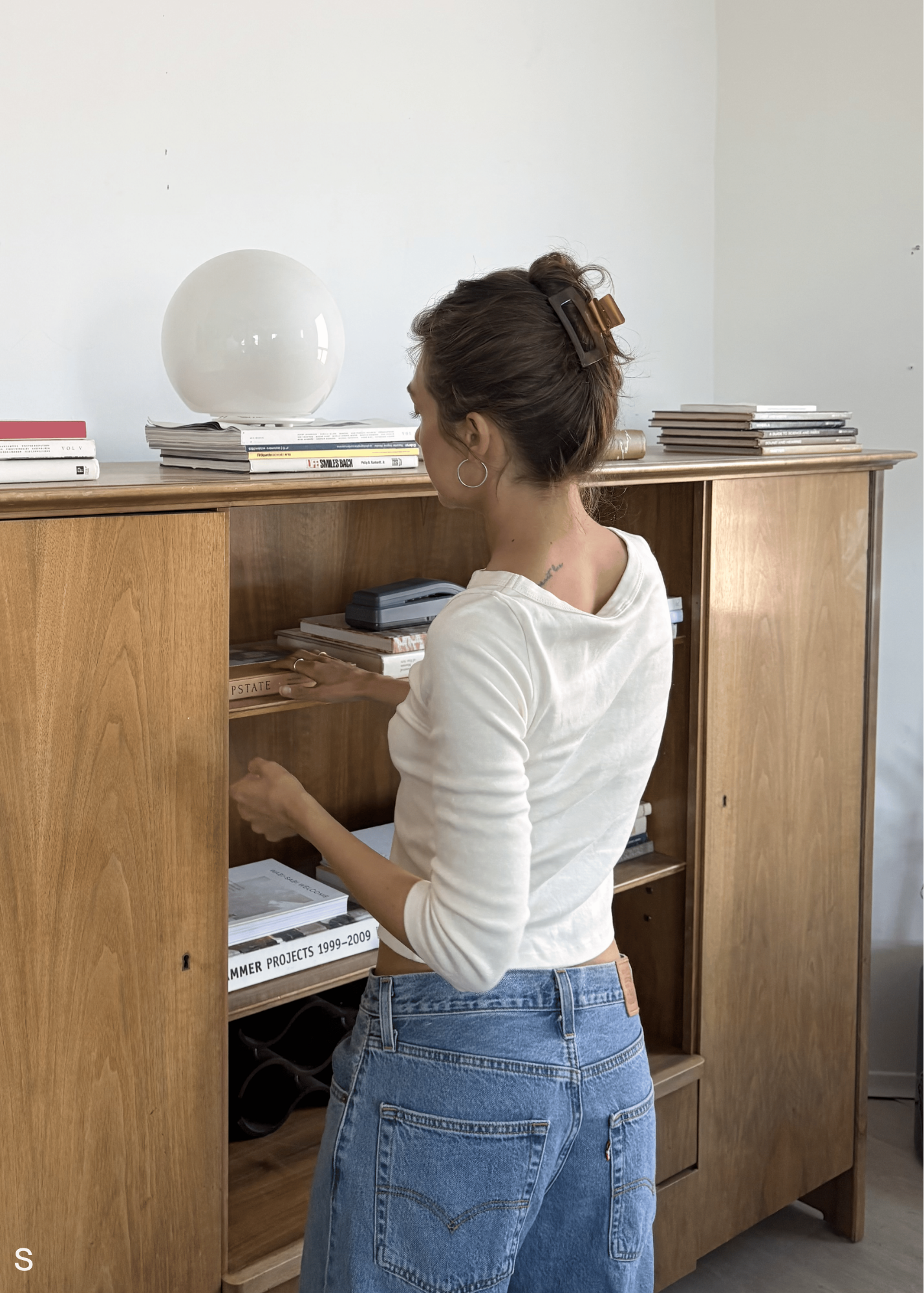 Woman organizing items inside a wooden cabinet wearing a caramel coloured hair clip.