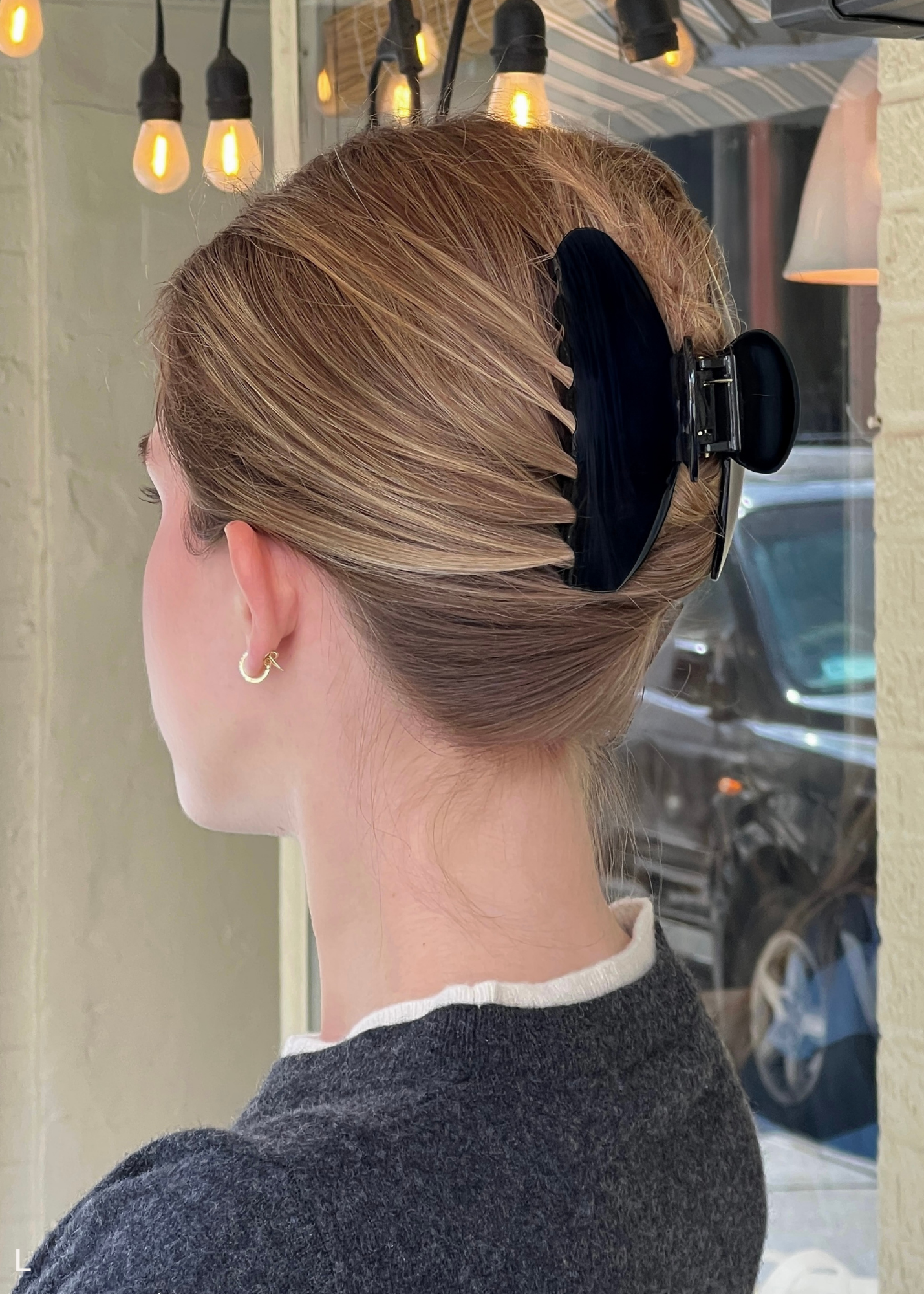 Person with a stylish hairdo featuring a large black hair clip, set against an urban background.