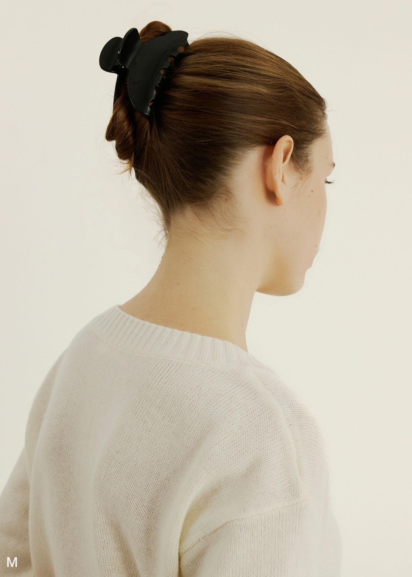 Woman with a medium sized black hair accessory in her bu.n on a light background