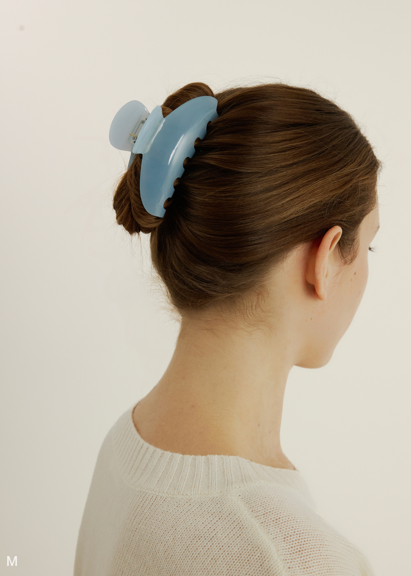 Woman with a light blue hair clip in her hair against a plain background.