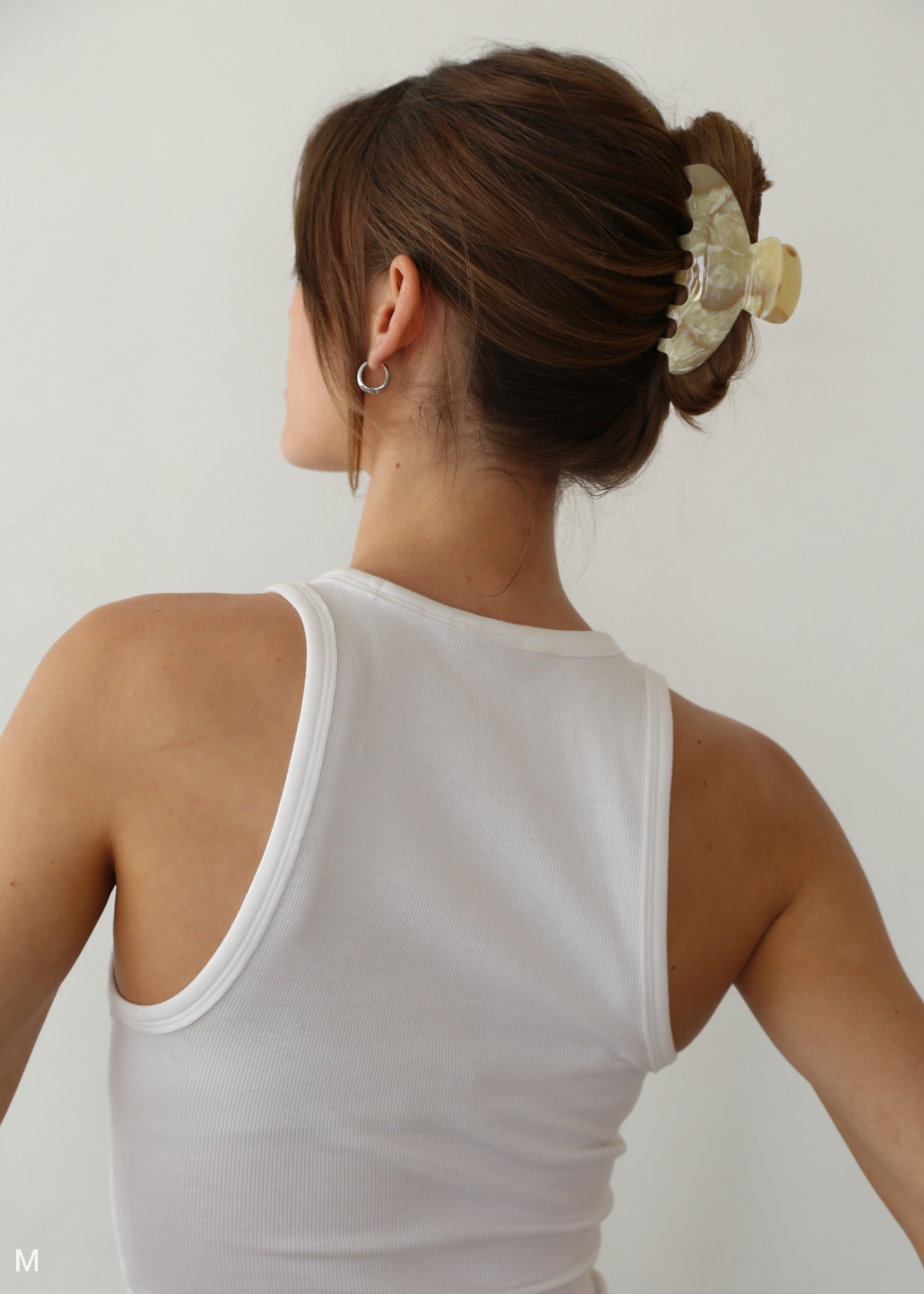 Woman wearing a cream claw clip against a plain background.