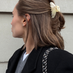 Women wearing a small cream claw clip with her hair half up in front of a stone wall.
