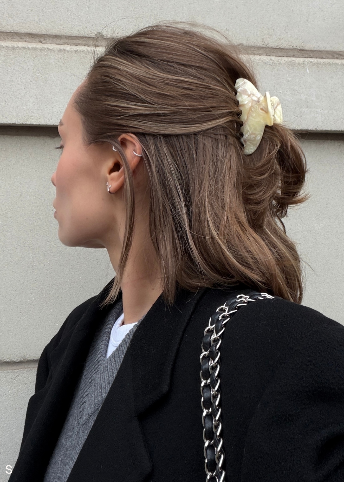 Women wearing a small cream claw clip with her hair half up in front of a stone wall.