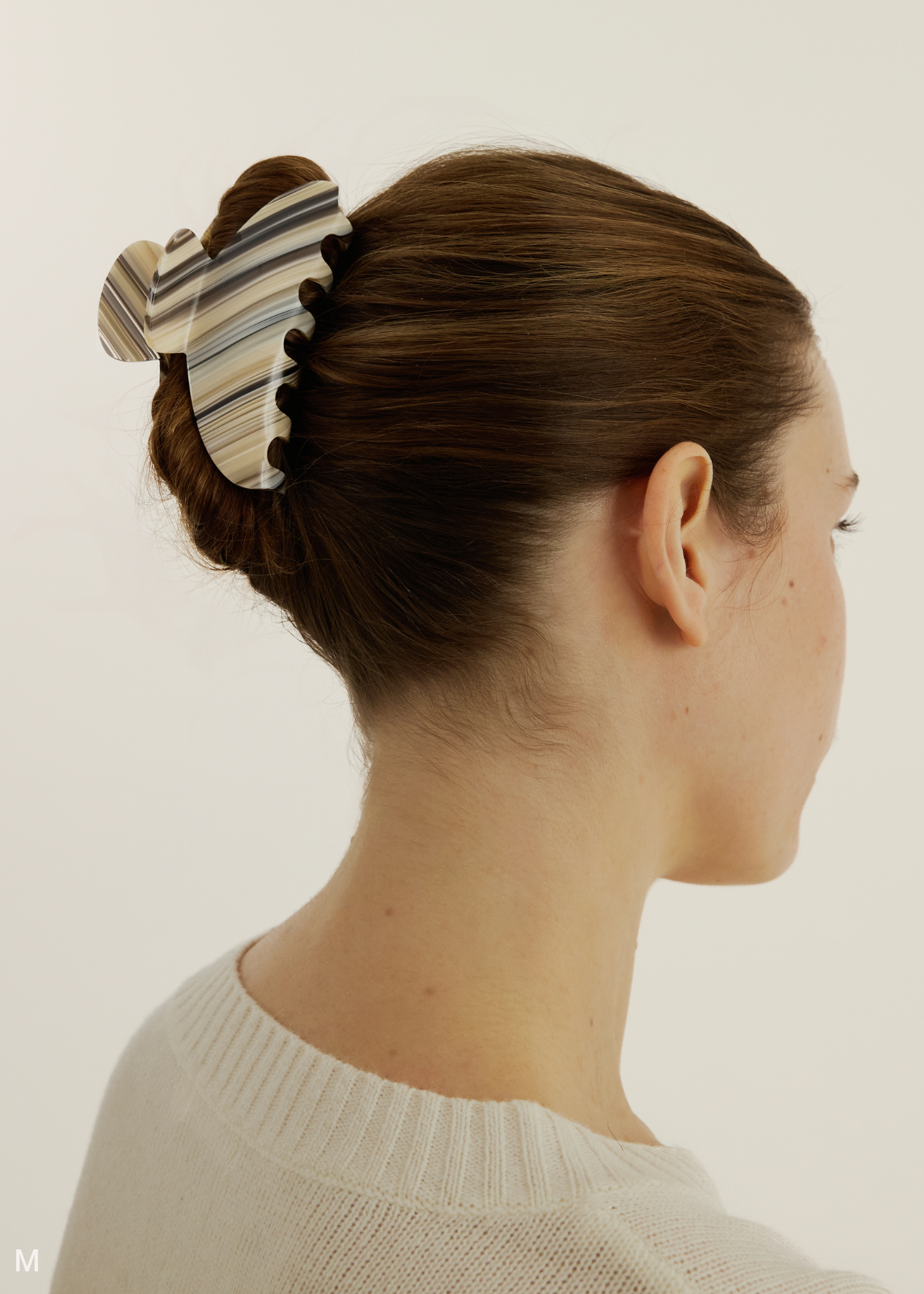 A striped pattern claw clip with beige, dark and light blue stripes on a person with brown hair on a white background