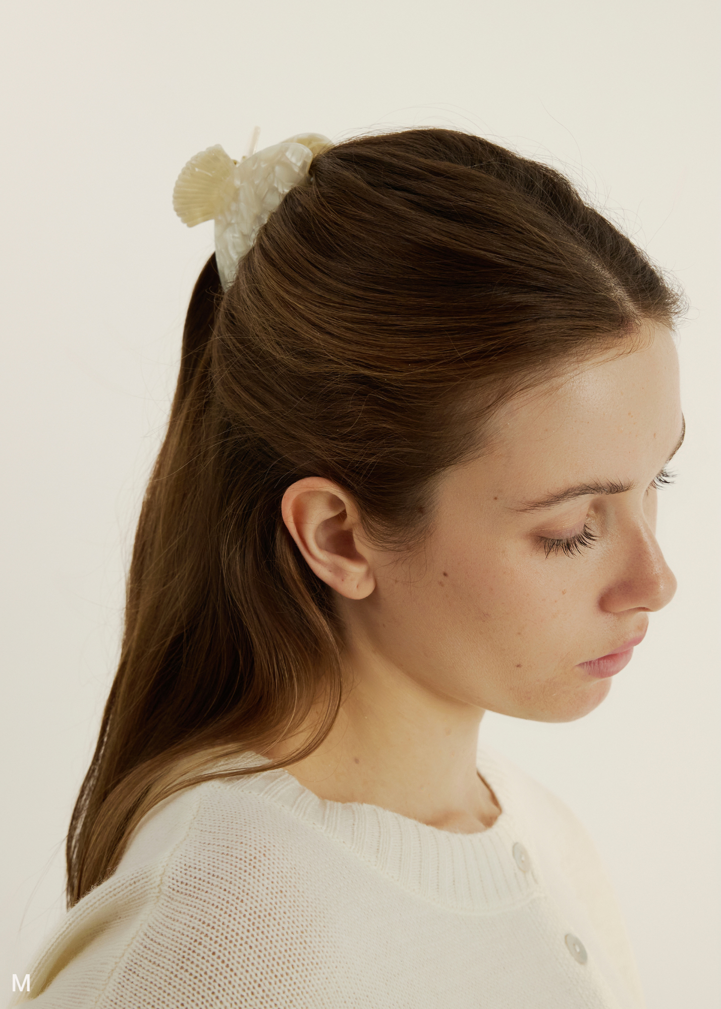 Woman with a mother of pearl hair clip with shell detailing worn in her hair half up on a plain background.