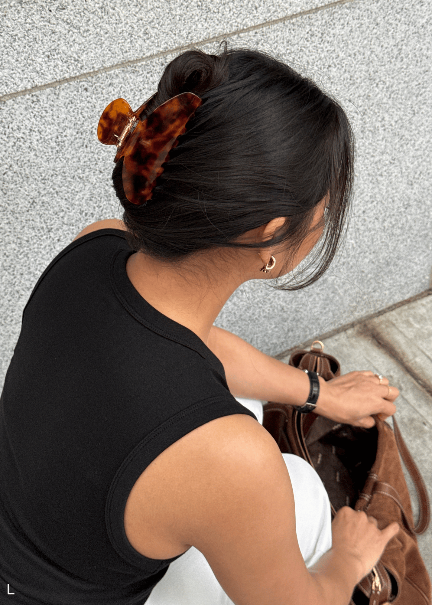 Person wearing a large tortoiseshell claw clip bending over to look in their purse.