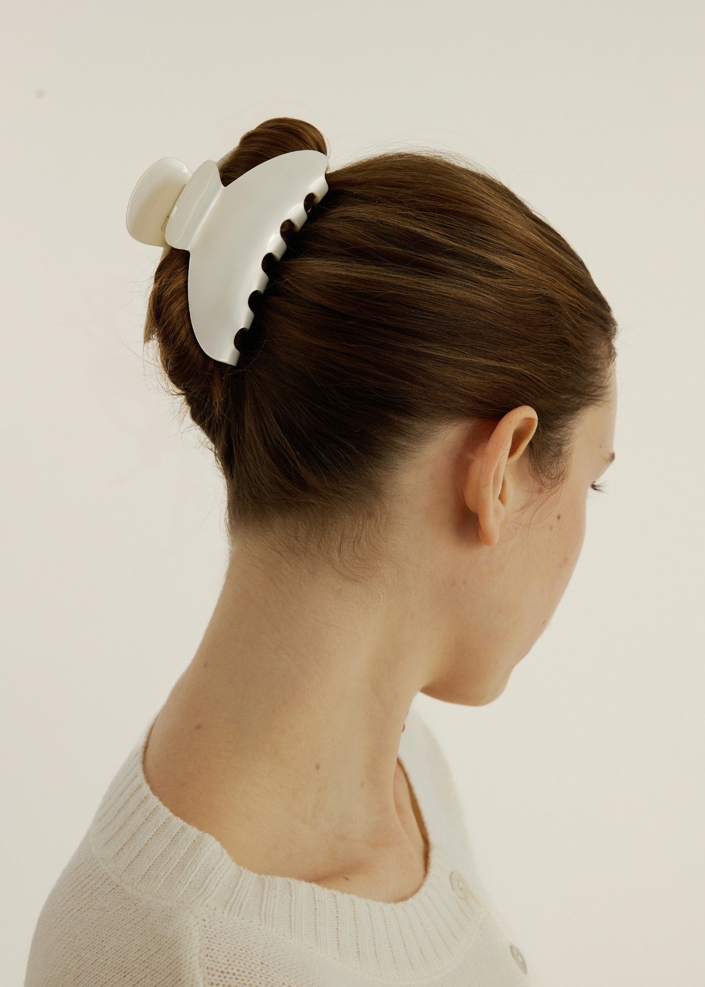 Side view of a woman with blonde hair wearing a large pearl coloured hair claw clip to secure her up do hairstyle