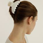 Side view of a woman with blonde hair wearing a large pearl coloured hair claw clip to secure her up do hairstyle