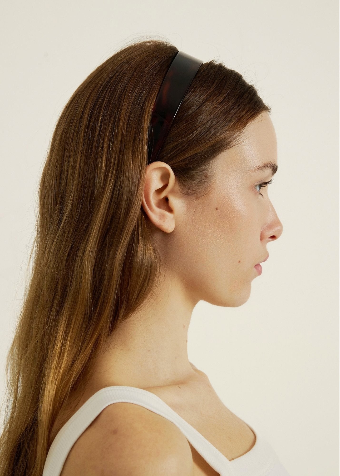 Woman with long hair wearing a dark reddish headband against a plain background