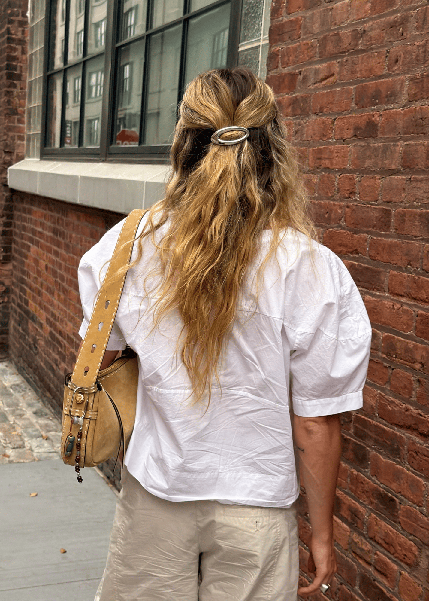 A woman viewed from behind wearing a metal barrette with a cutout in the middle to secure her hair half up half down. 