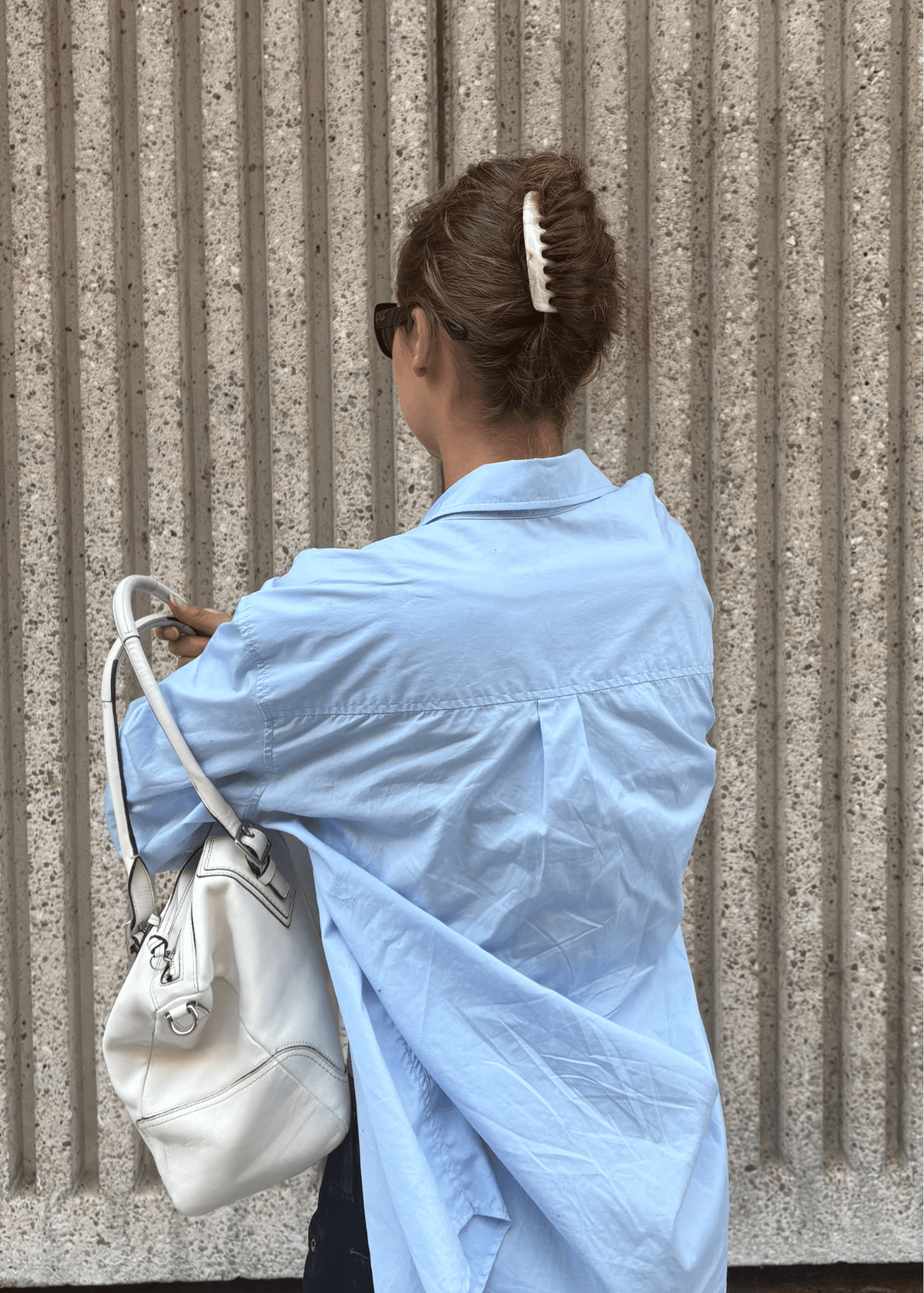 A woman, shown from the back, adjusts her purse on her shoulder. She wears a light neutral hair comb in her hair to secure her French twist updo.