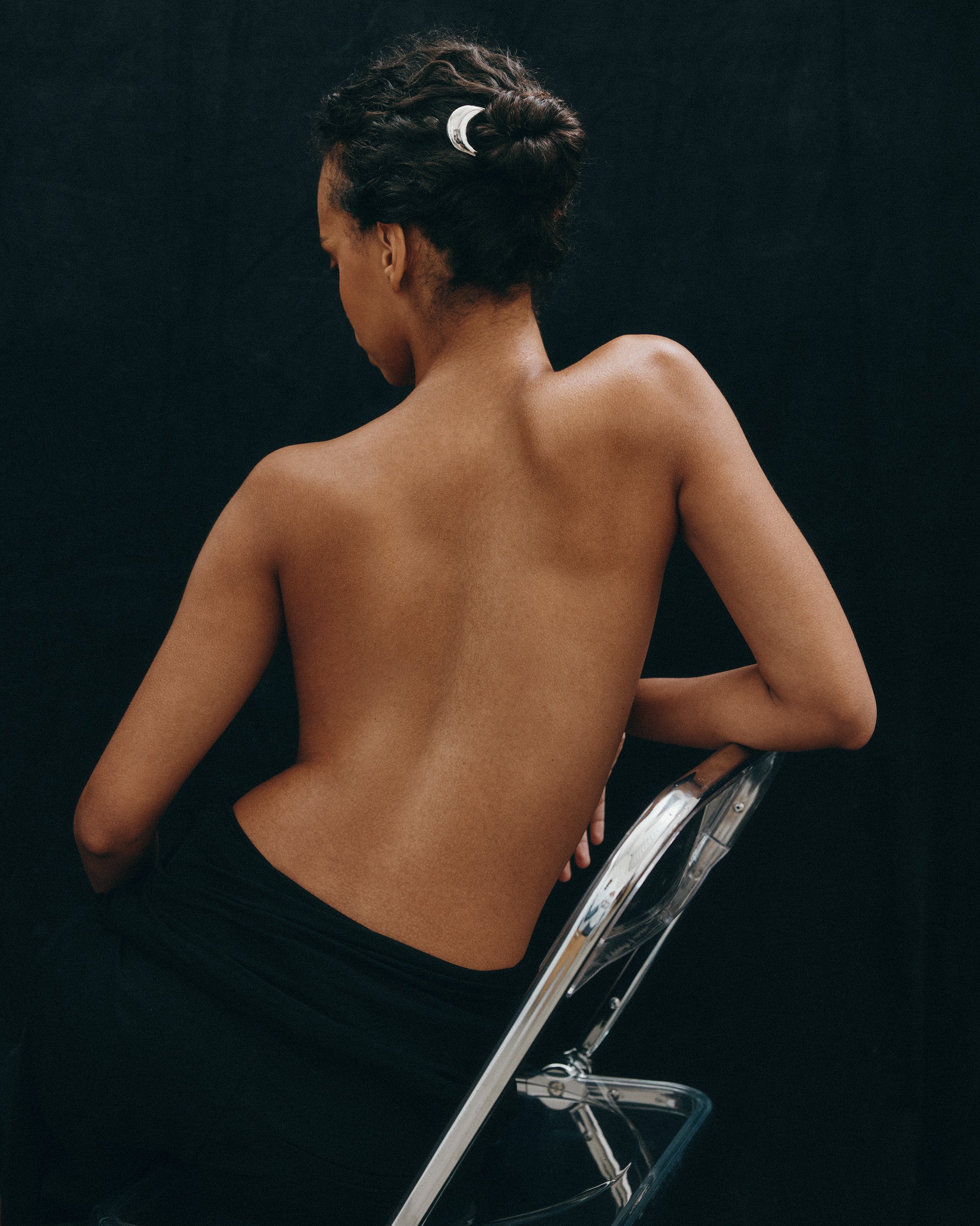 Woman sitting on a silver chair wearing the French Pin in Silver with a black background