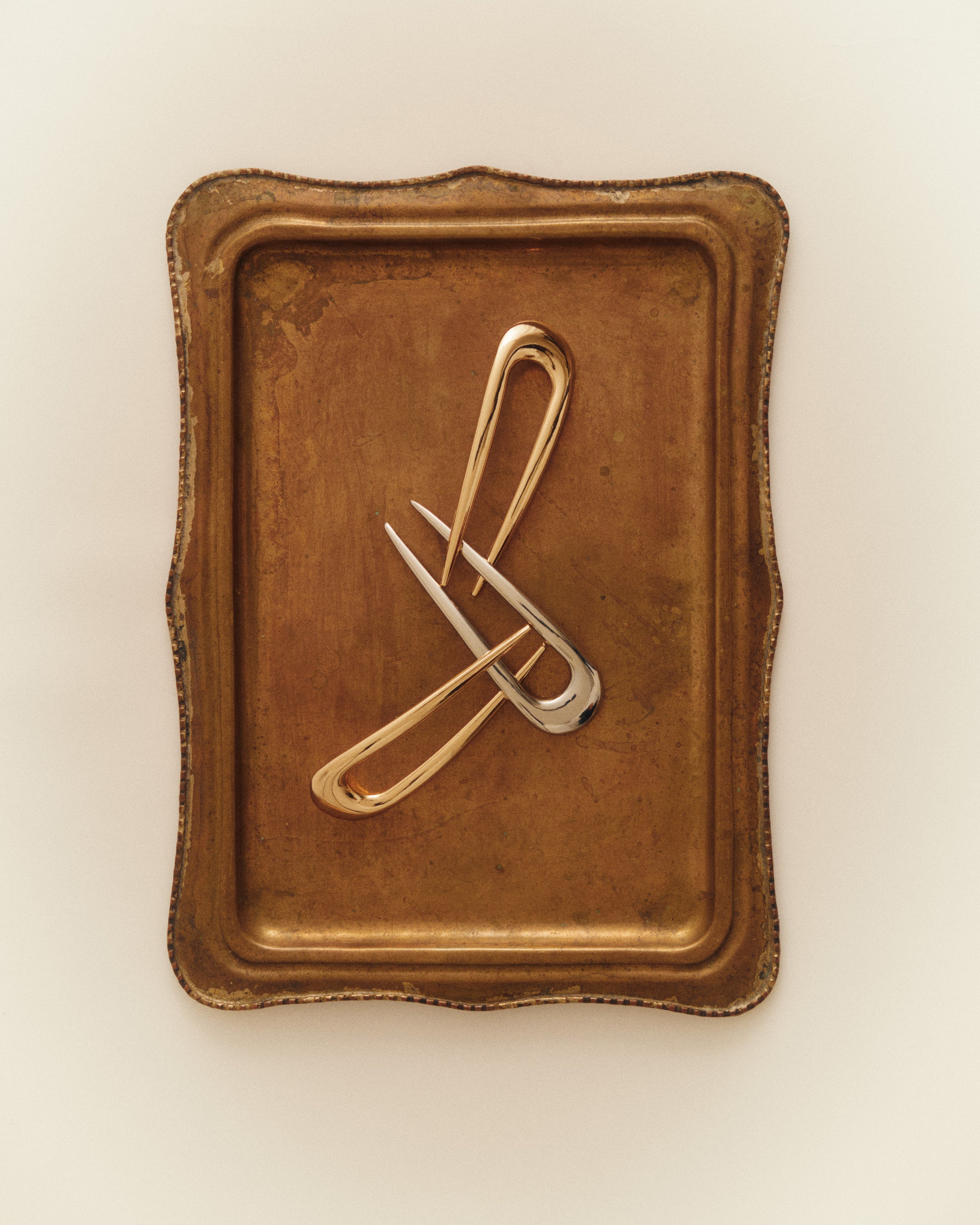 Two French pins in gold and one French Pin in Silver brown rectangular tray against a beige background