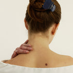 Woman with a bun secured with a navy blue hair clip on a plain background
