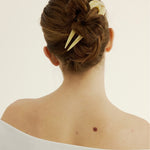 Back view of a person with a stylish hair bun and cream decorative hairpin on a plain background.