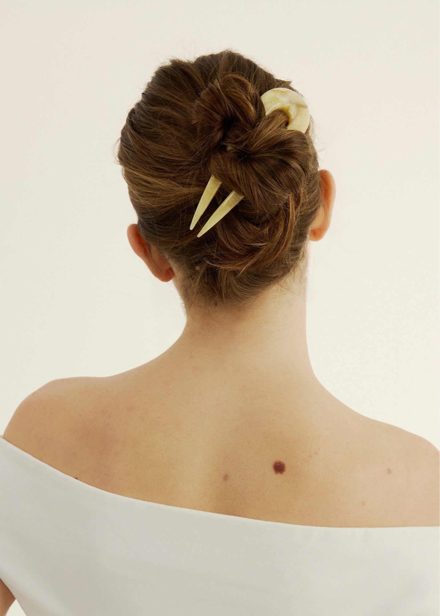 Back view of a person with a stylish hair bun and cream decorative hairpin on a plain background.