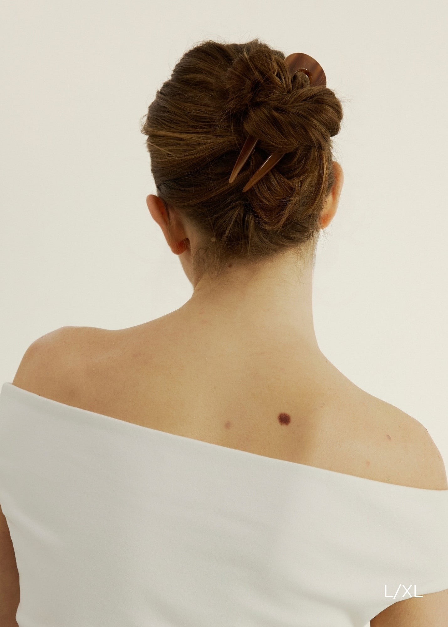 Person with a bun secured with the French Pin in Honey wearing a white tank top against a plain background