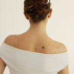 Back view of a woman with a stylish hair bun secured with a silver french pin wearing a white off-shoulder top with a neutral background