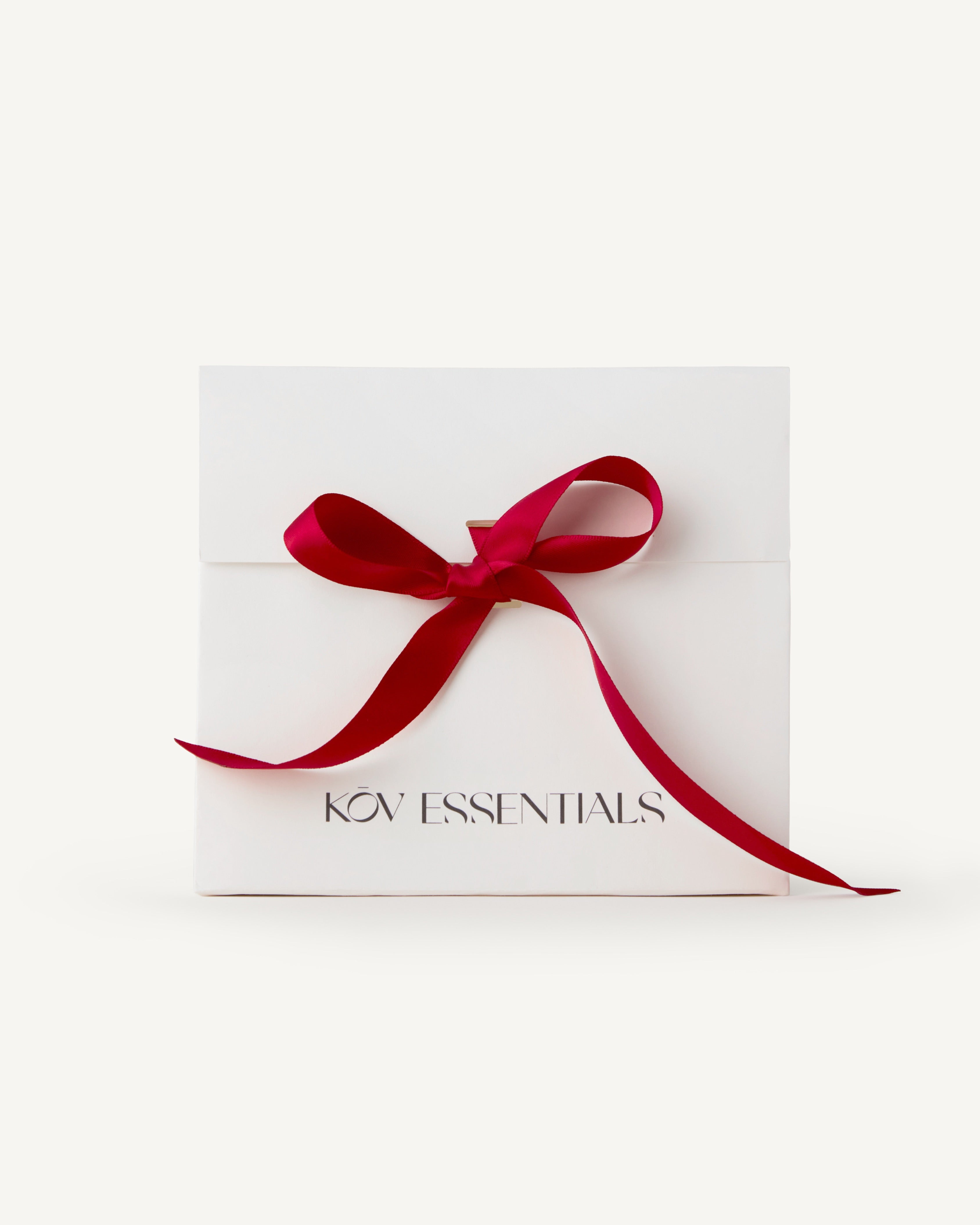 White holiday gift bag with a red ribbon and 'KOV ESSENTIALS' text on a white background