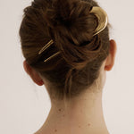 Person with a hair bun secured with the French Pin in gold against a white background