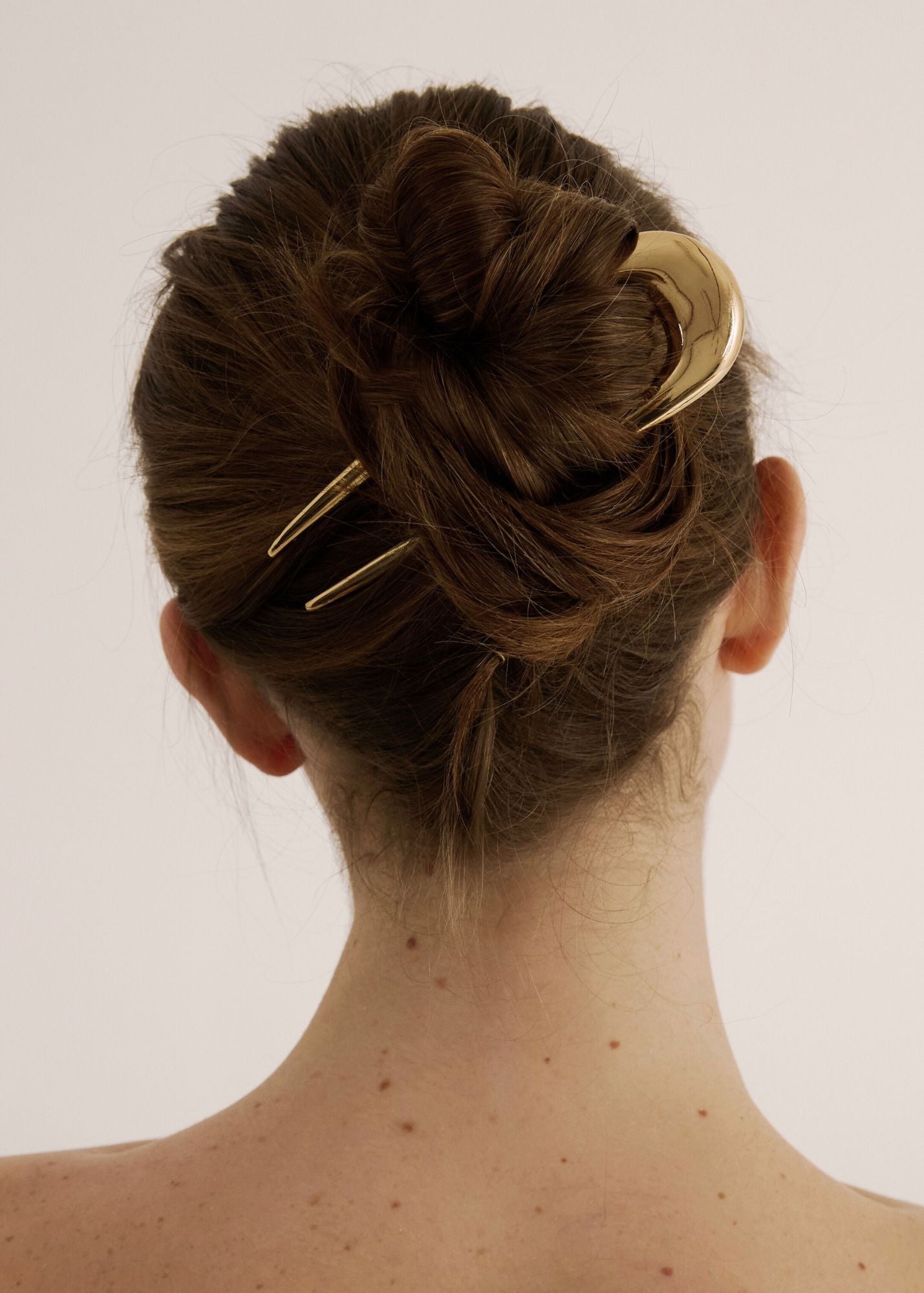 Person with a hair bun secured with the French Pin in gold against a white background