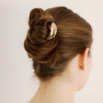 Back view of a woman with styled hair featuring the French pin in gold on a plain background