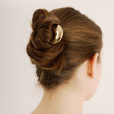 Back view of a woman with styled hair featuring the French pin in gold on a plain background