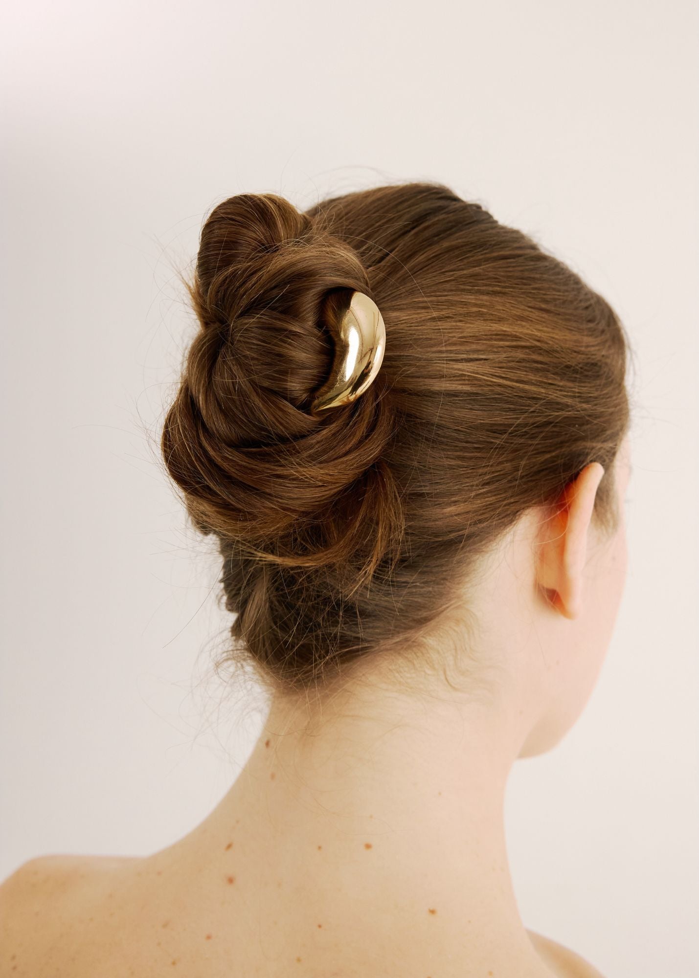 Back view of a woman with styled hair featuring the French pin in gold on a plain background