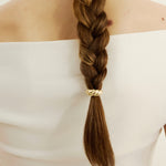 Braided hair with a gold croissant-shaped hair accessory on a plain background