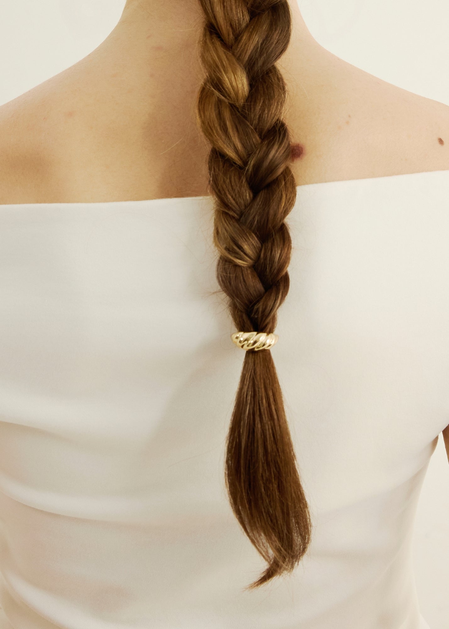 Braided hair with a gold croissant-shaped hair accessory on a plain background