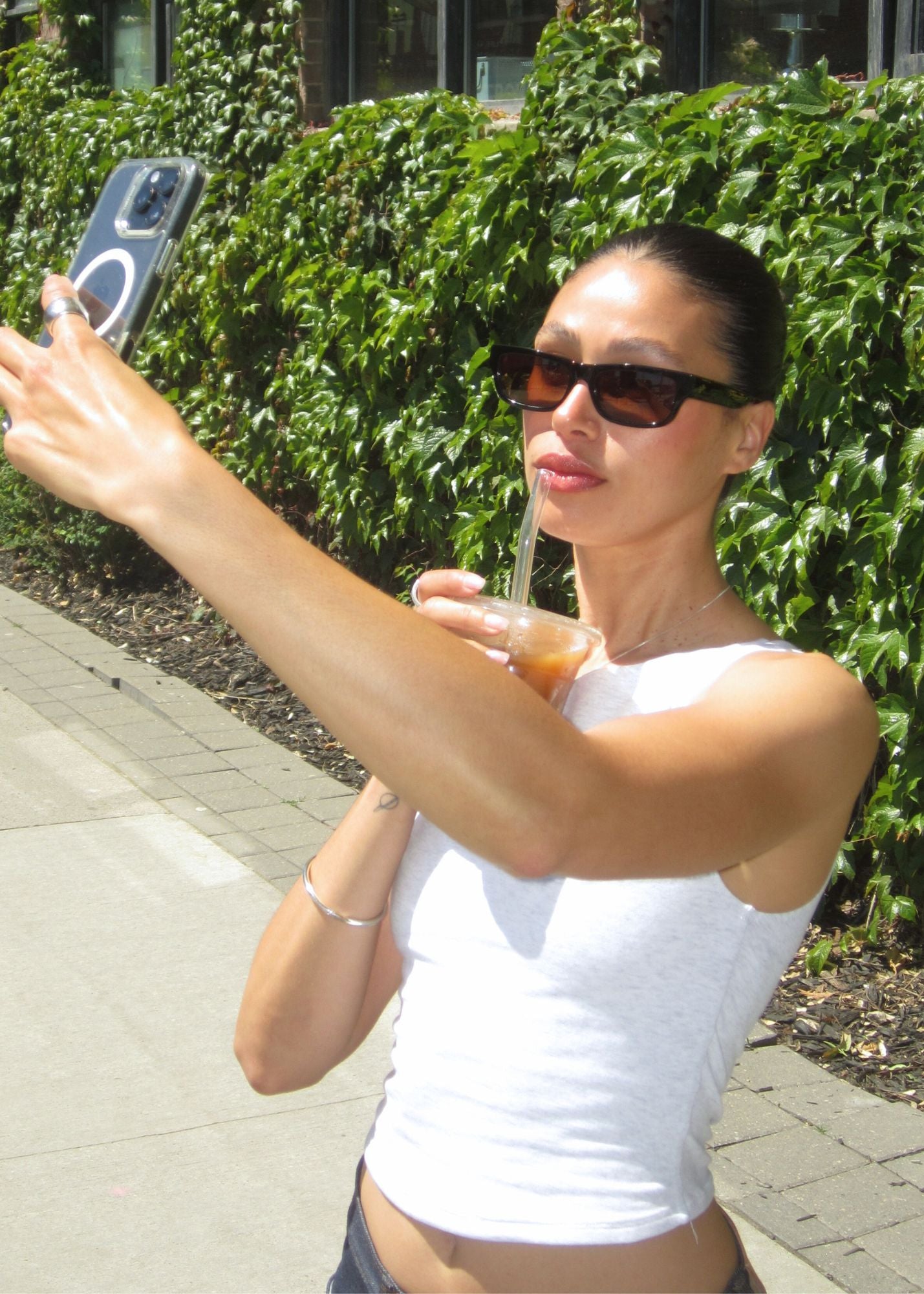 Woman taking a selfie outdoors wearing the Haven sunglasses in black with brown lenses and greenery in the background