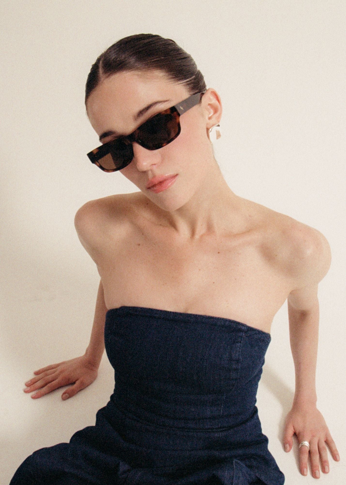 Woman wearing the Haven sunglasses in tortoise and a strapless navy dark denim top against a plain background